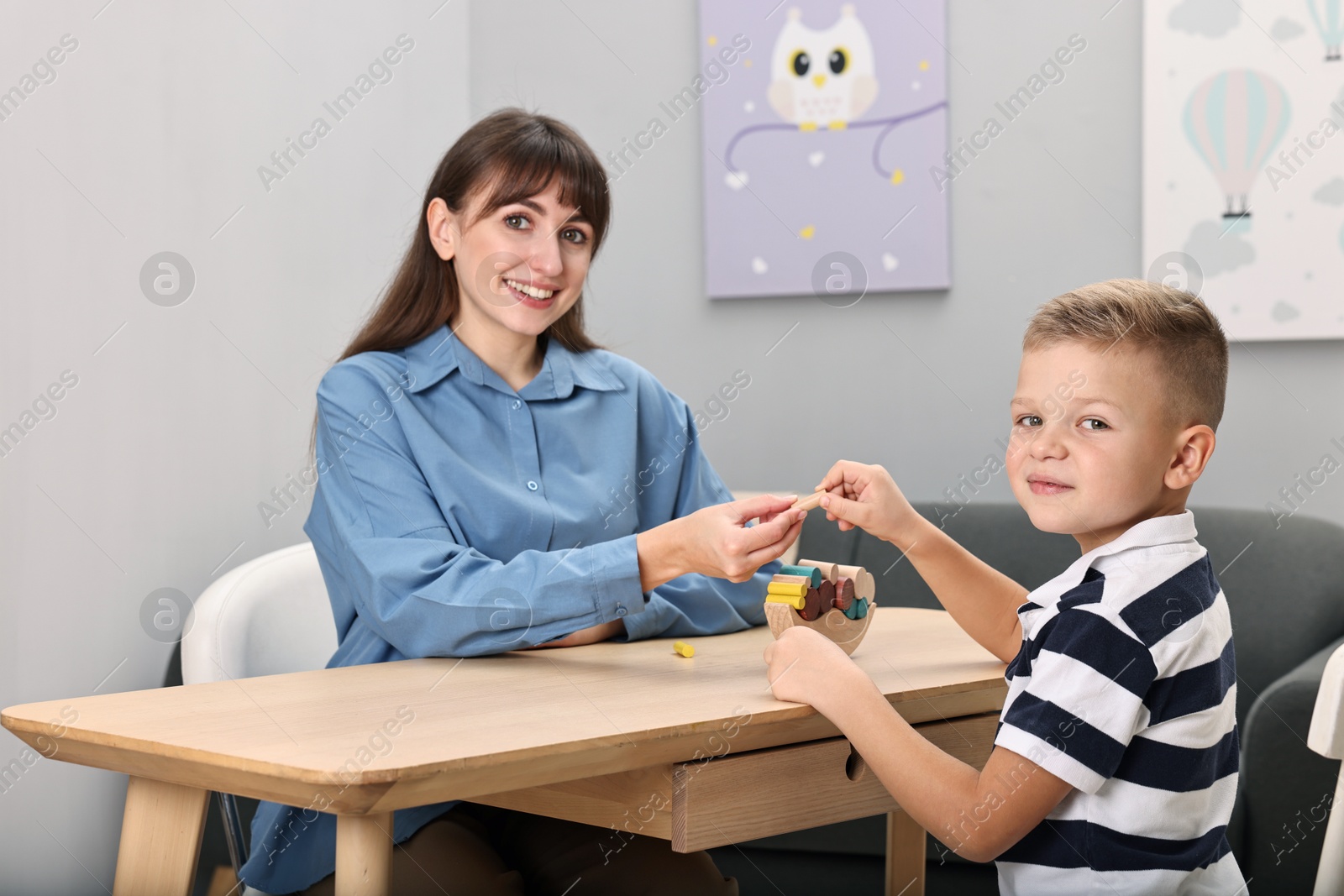 Photo of Autism therapy. Smiling psychologist and little boy playing with educational toy at table in mental health center