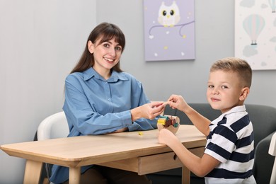 Photo of Autism therapy. Smiling psychologist and little boy playing with educational toy at table in mental health center