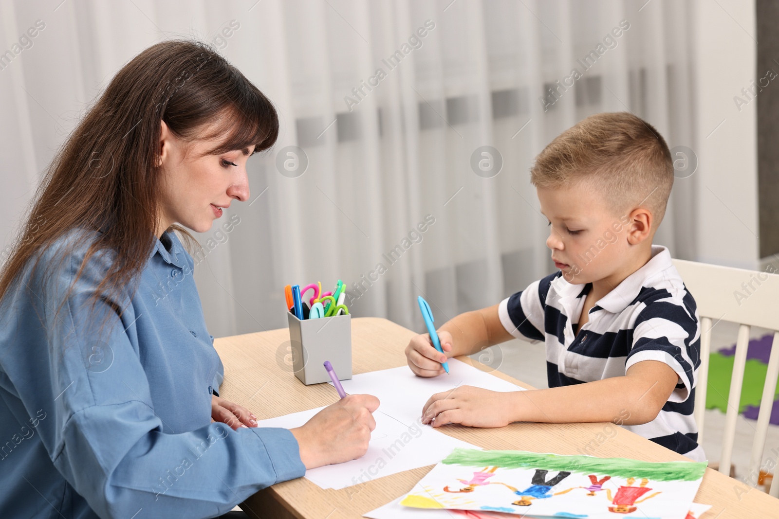 Photo of Autism therapy. Psychologist and little boy drawing pictures at table in mental health center