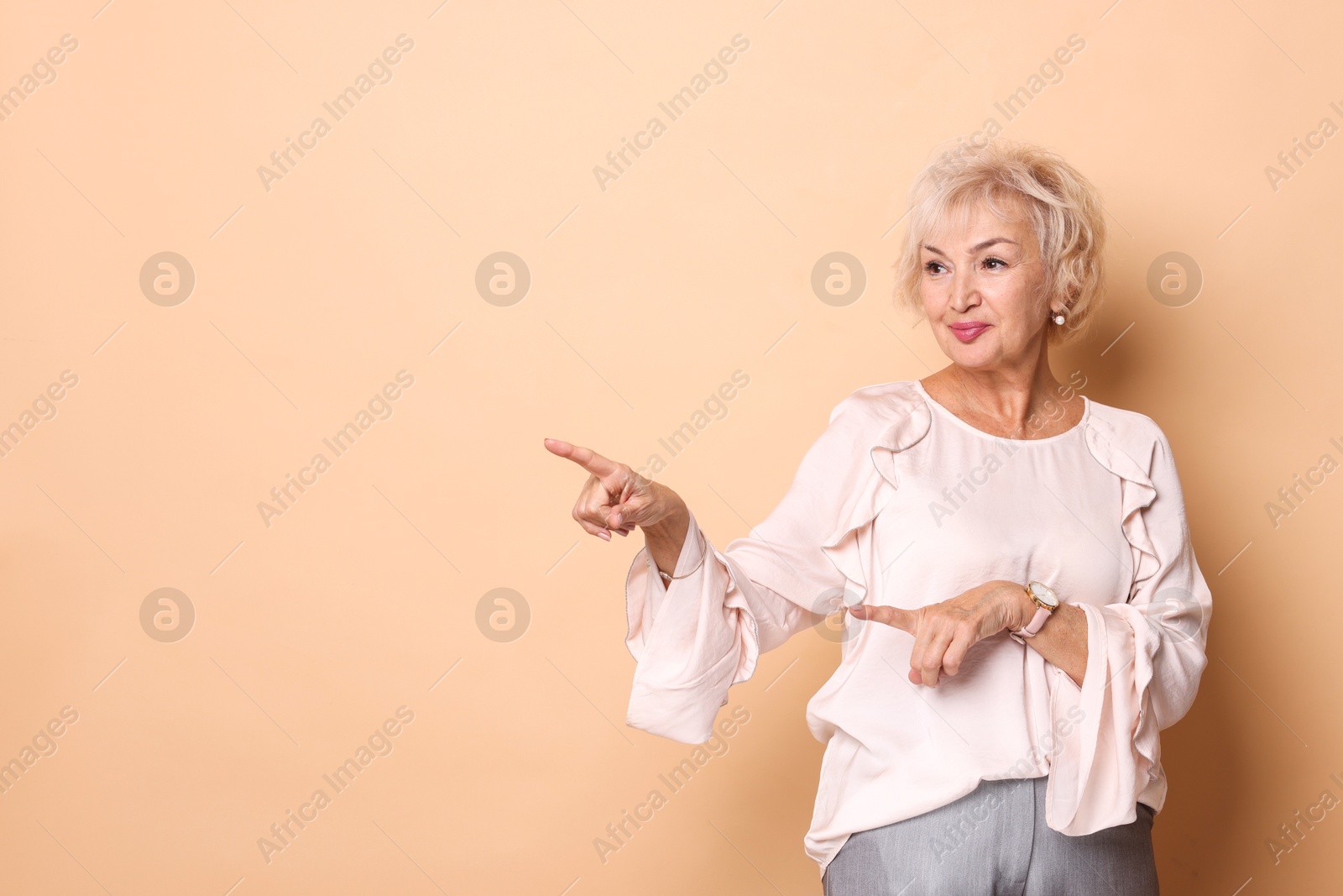 Photo of Beautiful grandmother pointing at something on beige background. Space for text