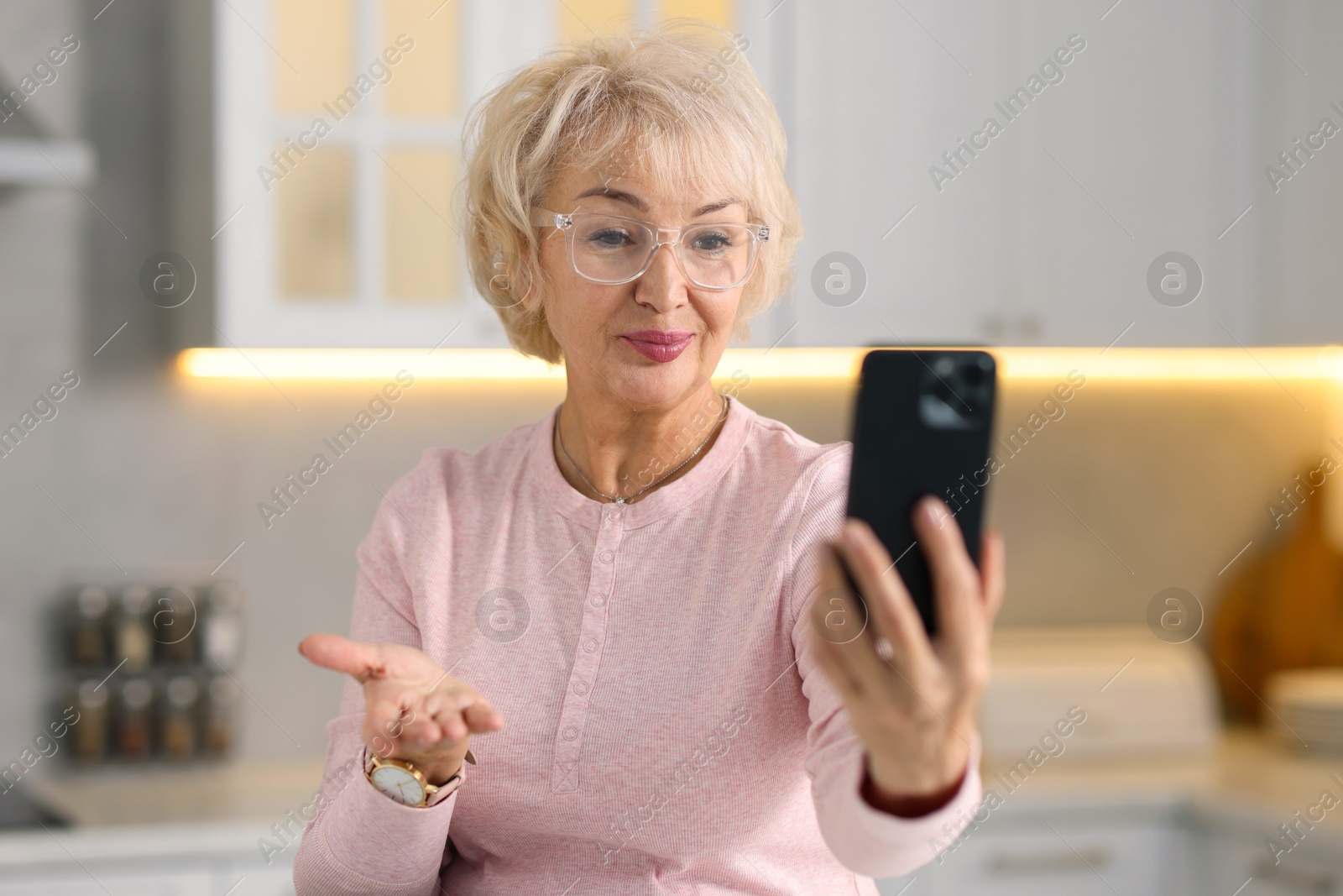 Photo of Beautiful grandmother having video chat via smartphone in kitchen, selective focus