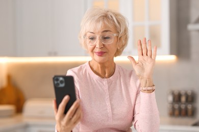 Beautiful grandmother having video chat via smartphone in kitchen, selective focus