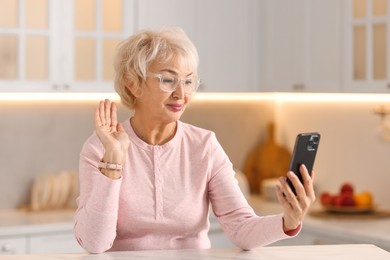 Beautiful grandmother having video chat via smartphone in kitchen