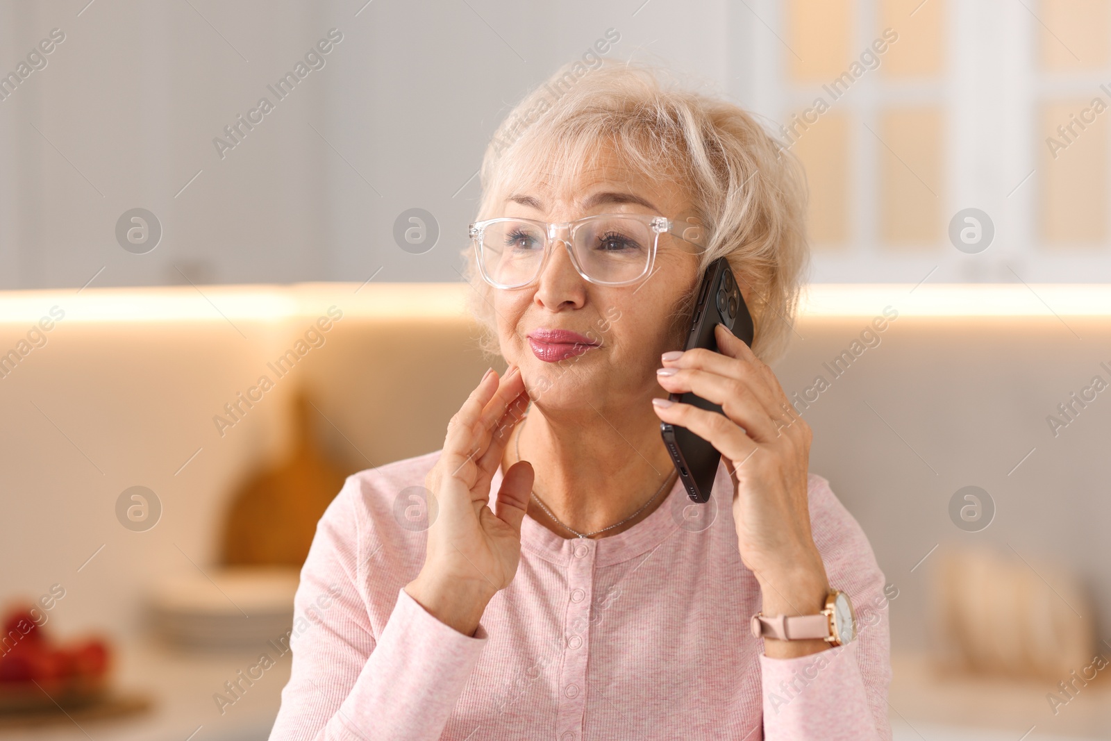 Photo of Beautiful grandmother talking on smartphone in kitchen