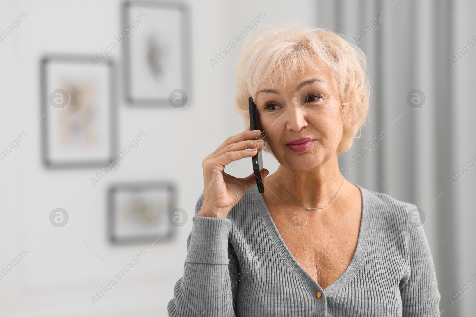 Photo of Beautiful grandmother talking on smartphone at home. Space for text