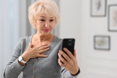 Beautiful grandmother using smartphone at home. Space for text