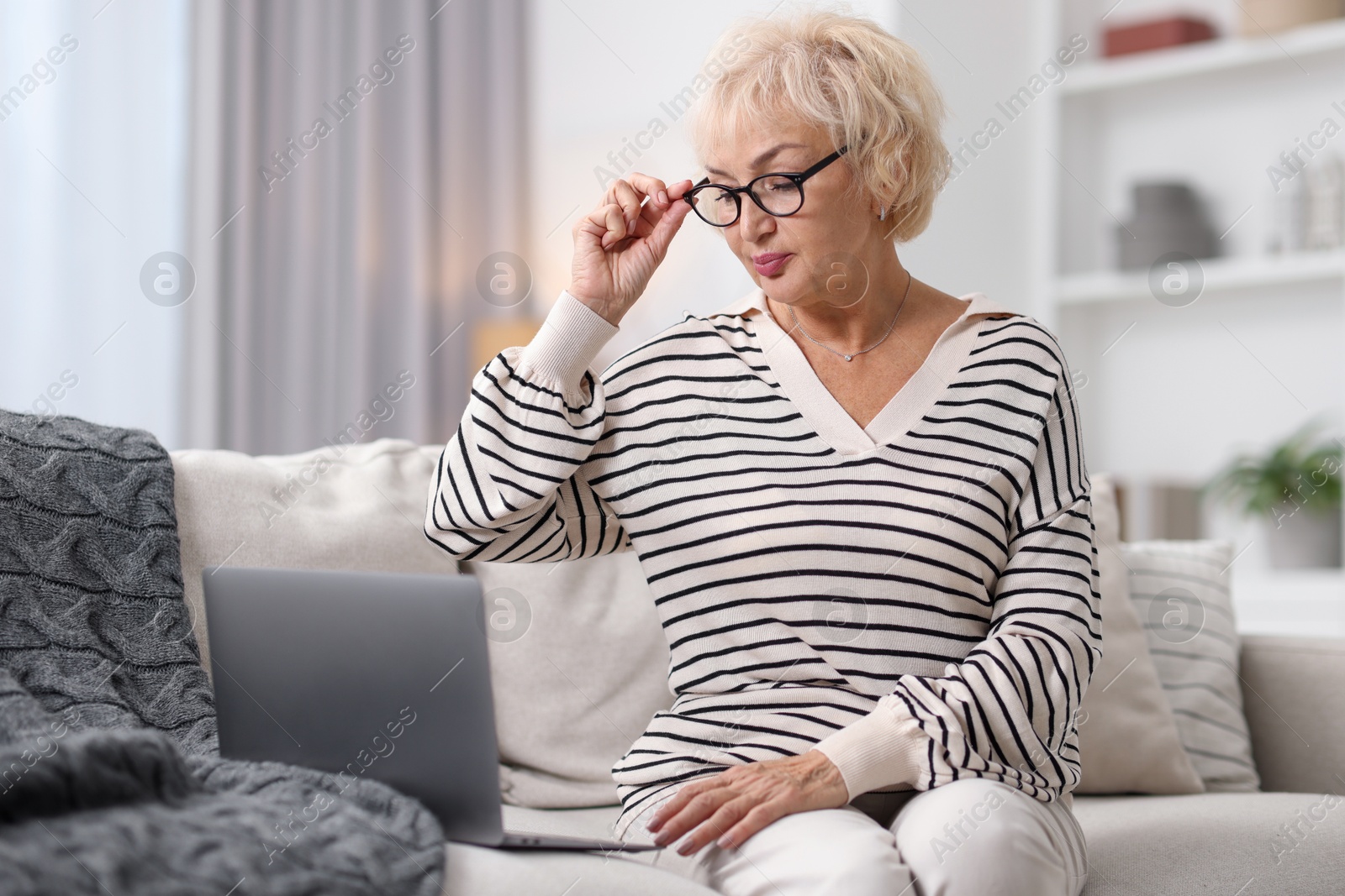 Photo of Beautiful grandmother using laptop on sofa at home