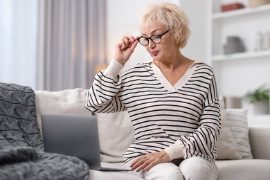 Photo of Beautiful grandmother using laptop on sofa at home