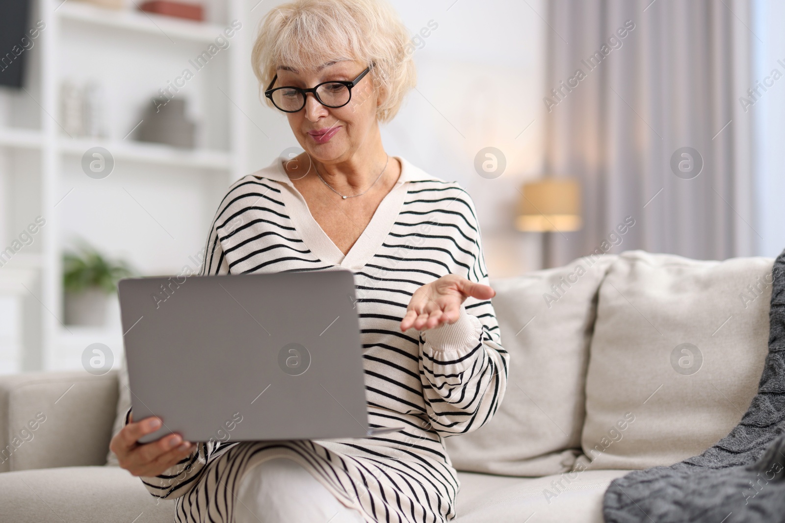 Photo of Beautiful grandmother using laptop on sofa at home