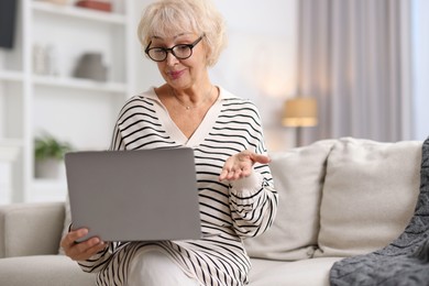 Photo of Beautiful grandmother using laptop on sofa at home