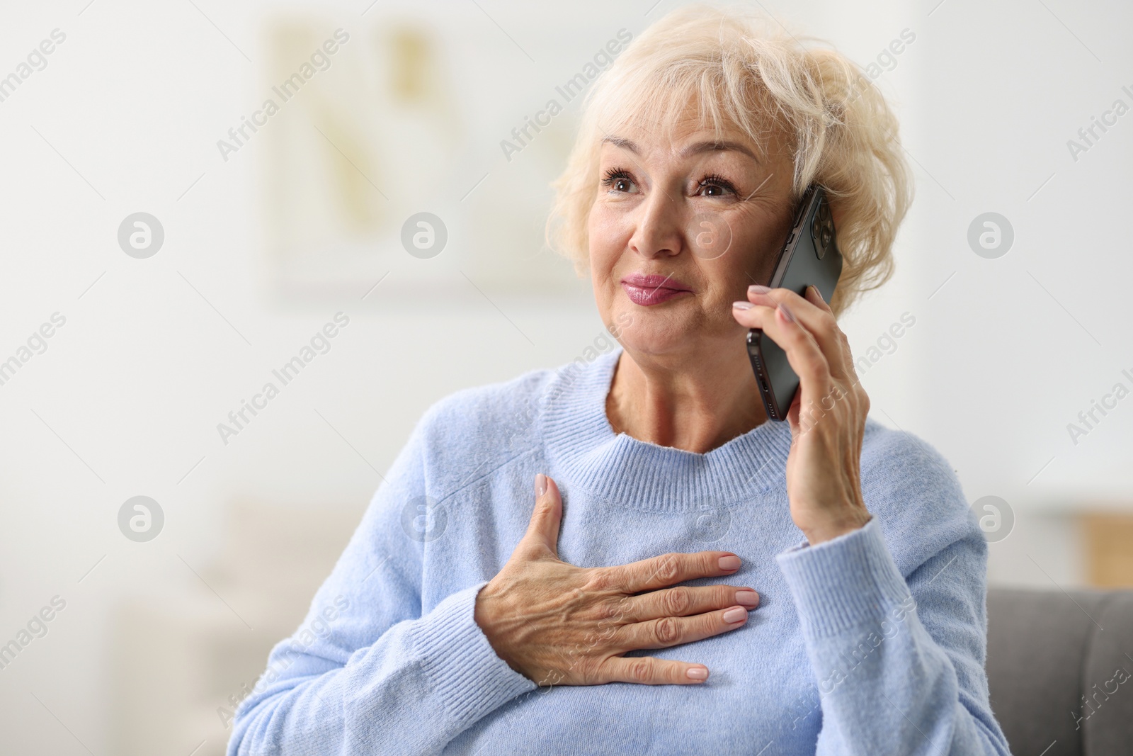 Photo of Beautiful grandmother talking on smartphone at home. Space for text