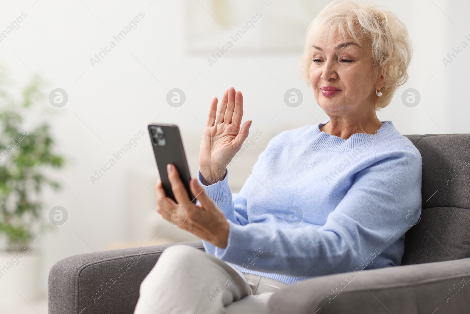 Photo of Beautiful grandmother having video chat via smartphone at home