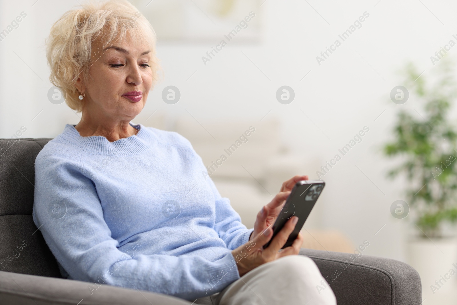 Photo of Beautiful grandmother using smartphone at home. Space for text