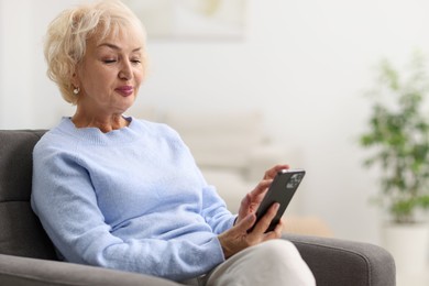 Photo of Beautiful grandmother using smartphone at home. Space for text