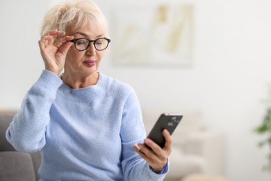 Photo of Beautiful grandmother using smartphone at home. Space for text