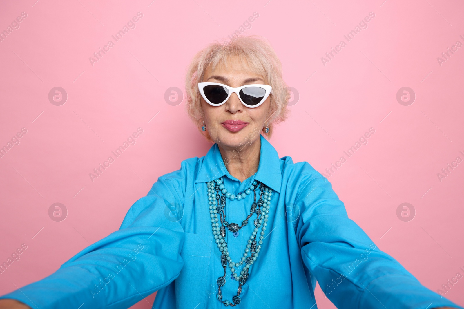 Photo of Fashionable grandmother taking selfie on pink background