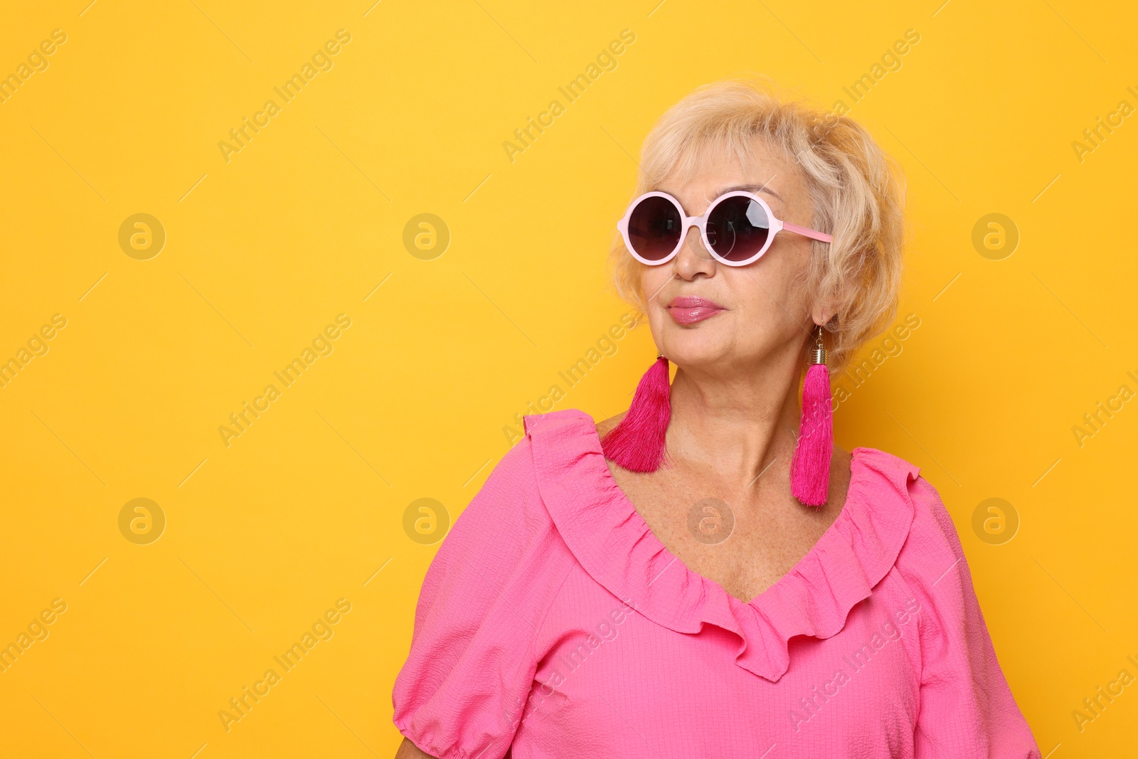 Photo of Portrait of fashionable grandmother in sunglasses on orange background. Space for text