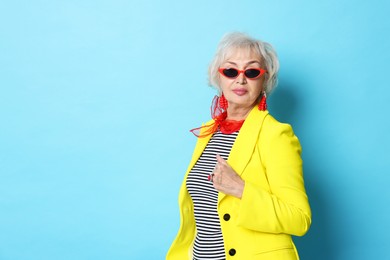 Portrait of fashionable grandmother in sunglasses and yellow jacket on light blue background. Space for text