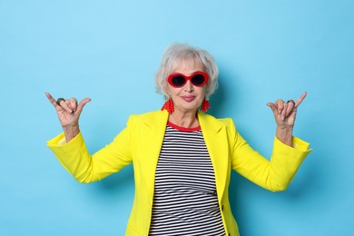 Photo of Cool grandmother in sunglasses showing shaka gesture on light blue background