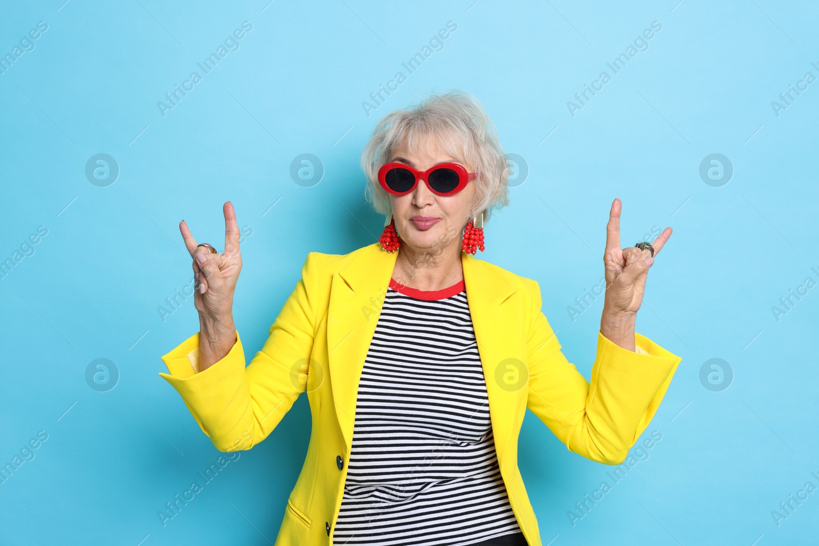 Photo of Cool grandmother showing rock gesture on light blue background