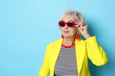 Portrait of fashionable grandmother in sunglasses and yellow jacket on light blue background. Space for text