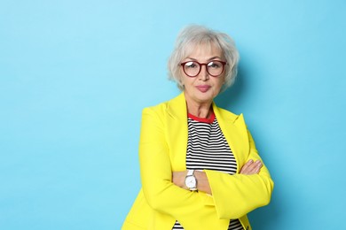 Portrait of grandmother in stylish yellow jacket on light blue background. Space for text