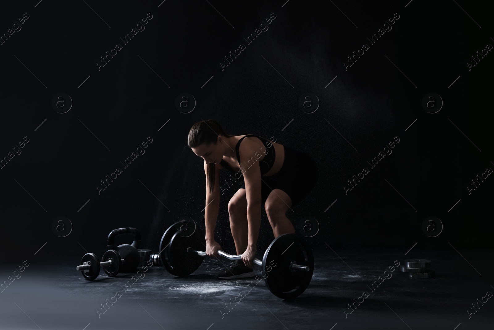 Photo of Woman training with barbell against black background