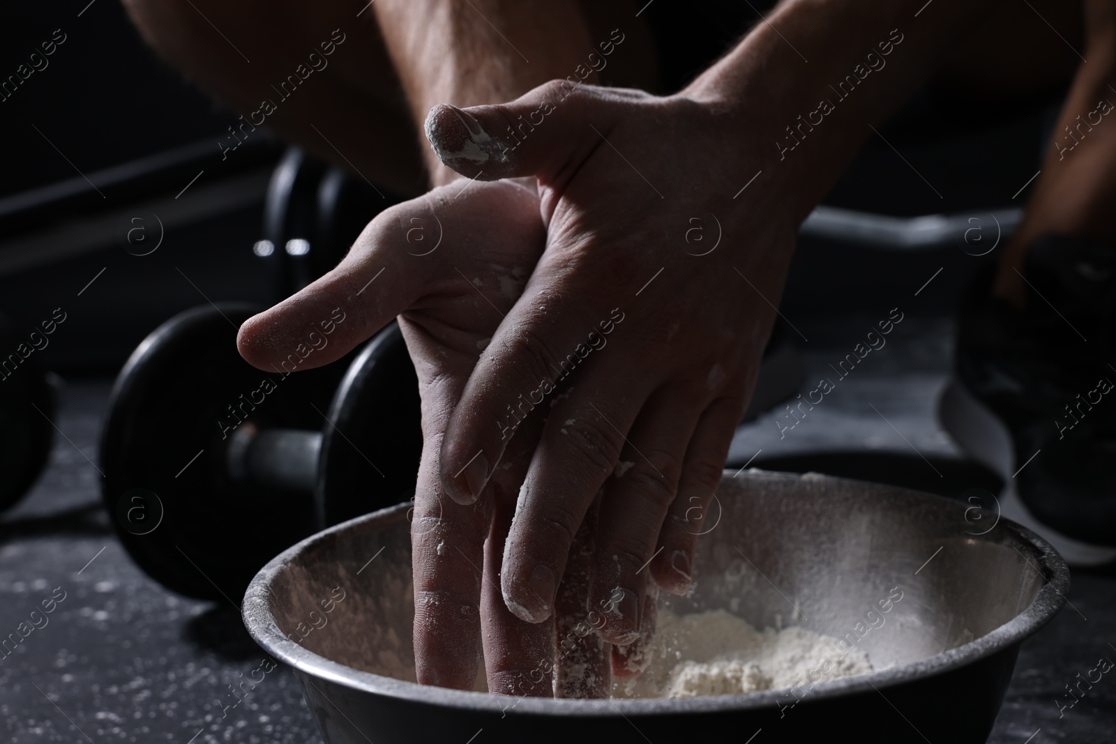 Photo of Man applying talcum powder onto his hands above bowl before training in gym, closeup