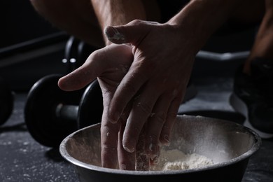 Photo of Man applying talcum powder onto his hands above bowl before training in gym, closeup