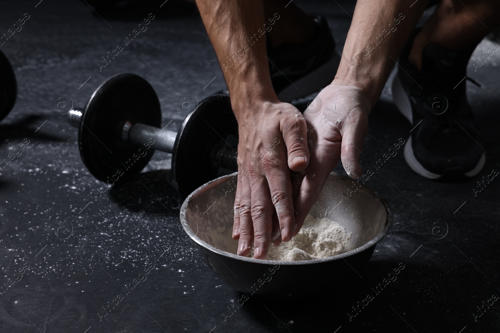 Photo of Man applying talcum powder onto his hands above bowl before training in gym, closeup