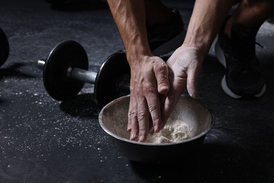 Photo of Man applying talcum powder onto his hands above bowl before training in gym, closeup