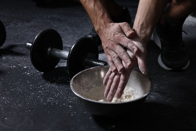 Photo of Man applying talcum powder onto his hands above bowl before training in gym, closeup