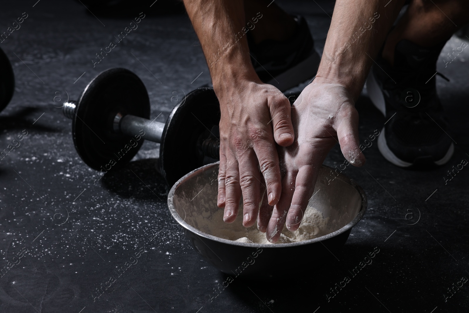 Photo of Man applying talcum powder onto his hands above bowl before training in gym, closeup