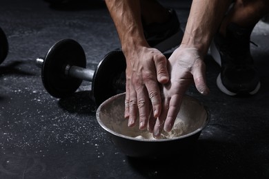 Photo of Man applying talcum powder onto his hands above bowl before training in gym, closeup