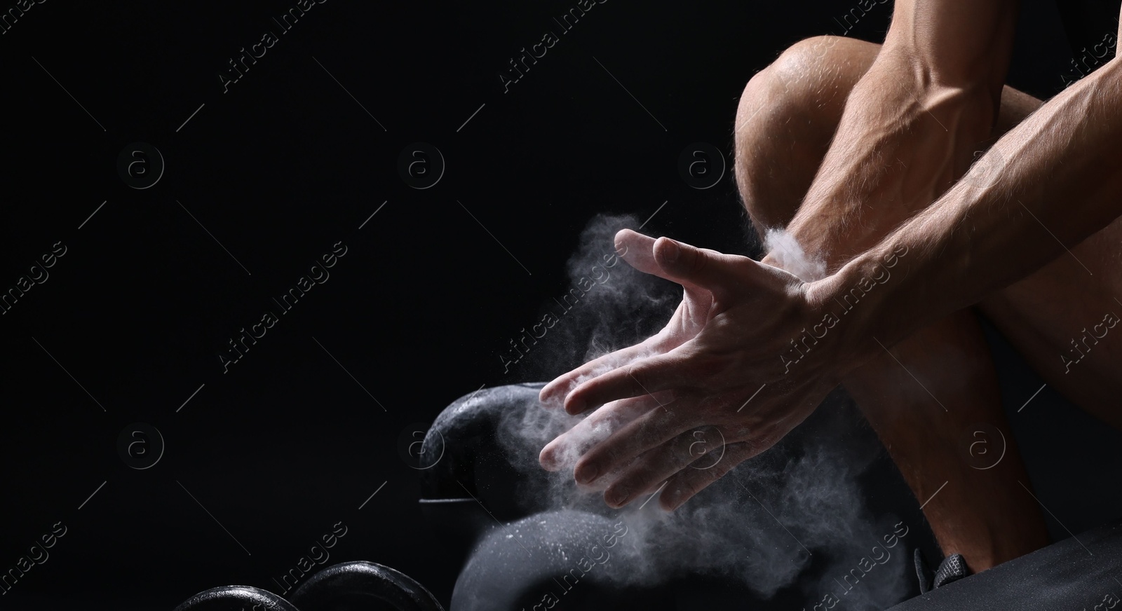 Photo of Man clapping hands with talcum powder above bowl before training on black background, closeup