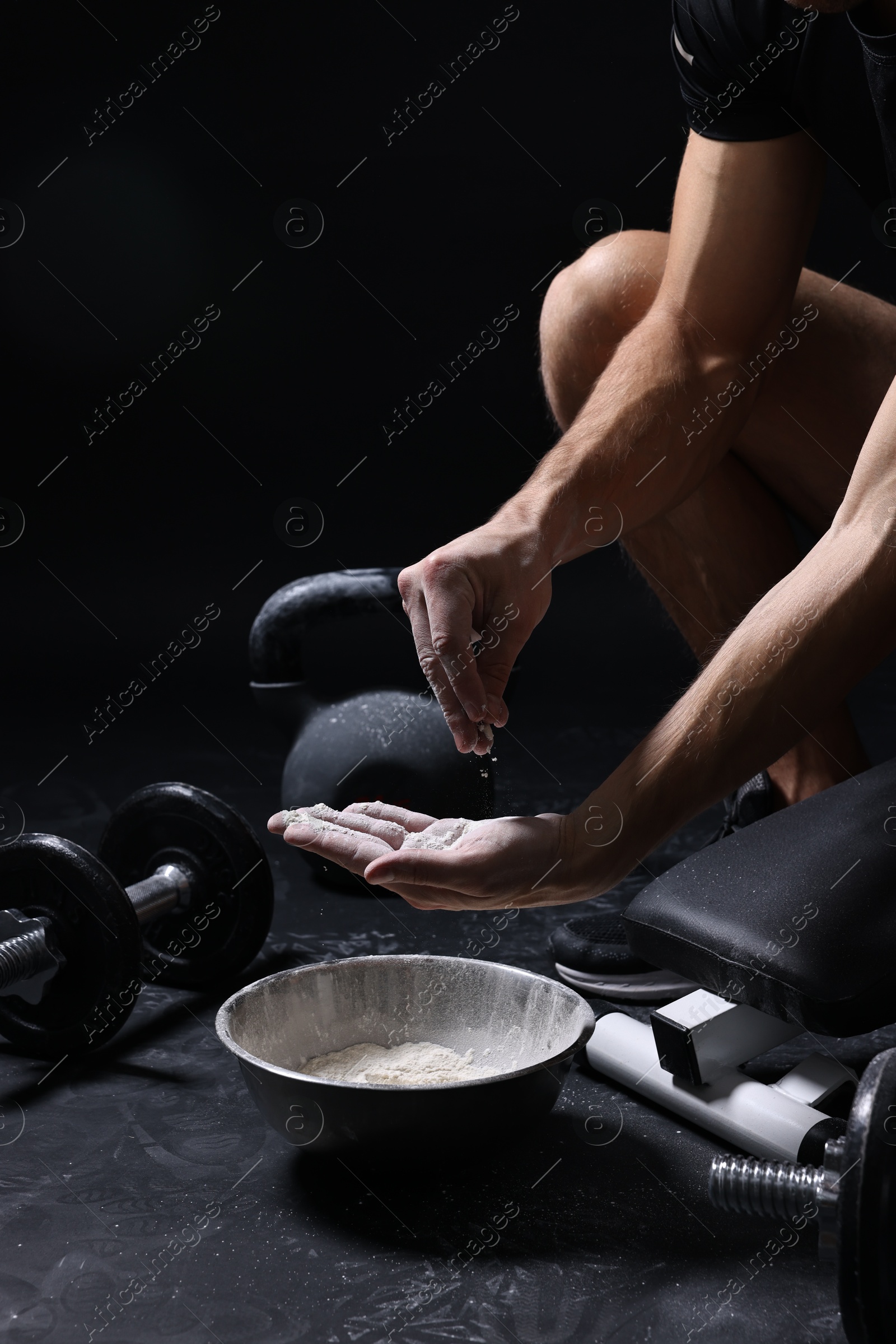 Photo of Man applying talcum powder onto his hands above bowl before training in gym, closeup