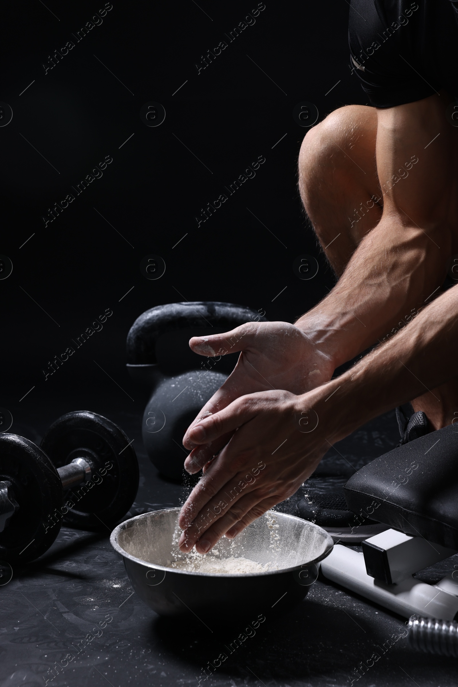 Photo of Man applying talcum powder onto his hands above bowl before training in gym, closeup