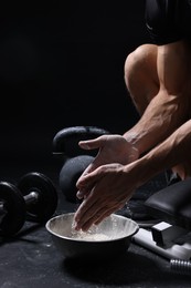 Photo of Man applying talcum powder onto his hands above bowl before training in gym, closeup