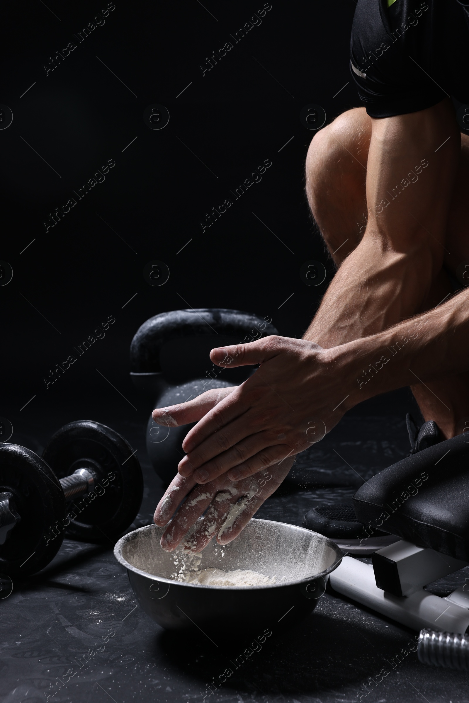 Photo of Man applying talcum powder onto his hands above bowl before training in gym, closeup