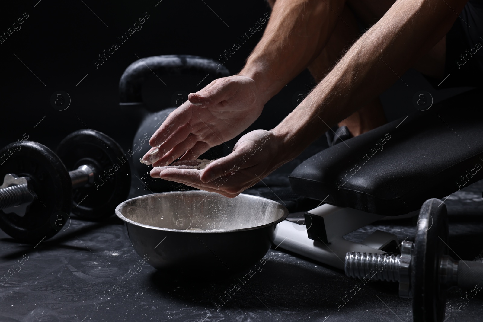 Photo of Man applying talcum powder onto his hands above bowl before training in gym, closeup