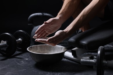 Photo of Man applying talcum powder onto his hands above bowl before training in gym, closeup