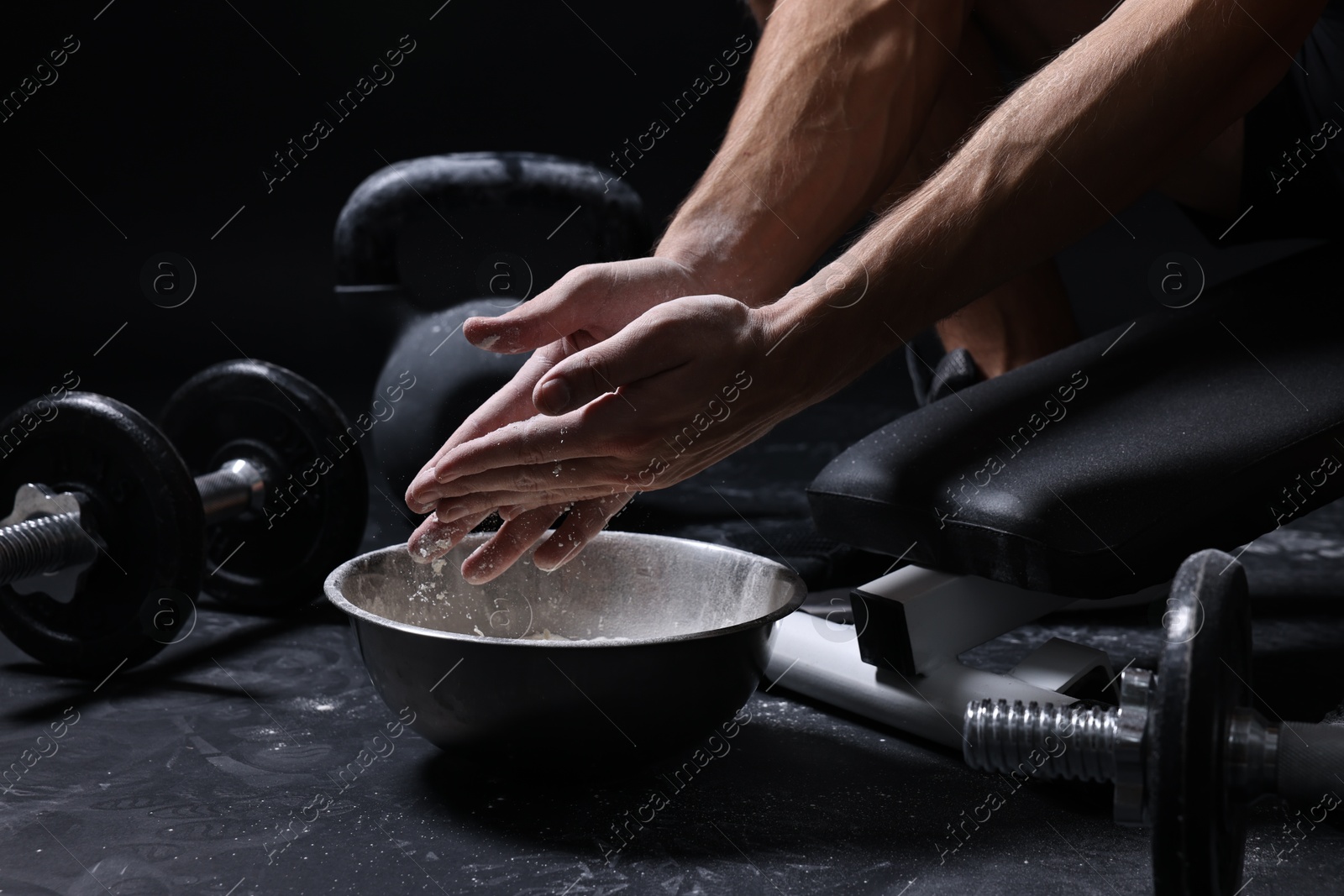 Photo of Man applying talcum powder onto his hands above bowl before training in gym, closeup