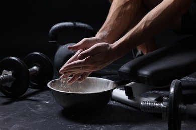 Photo of Man applying talcum powder onto his hands above bowl before training in gym, closeup