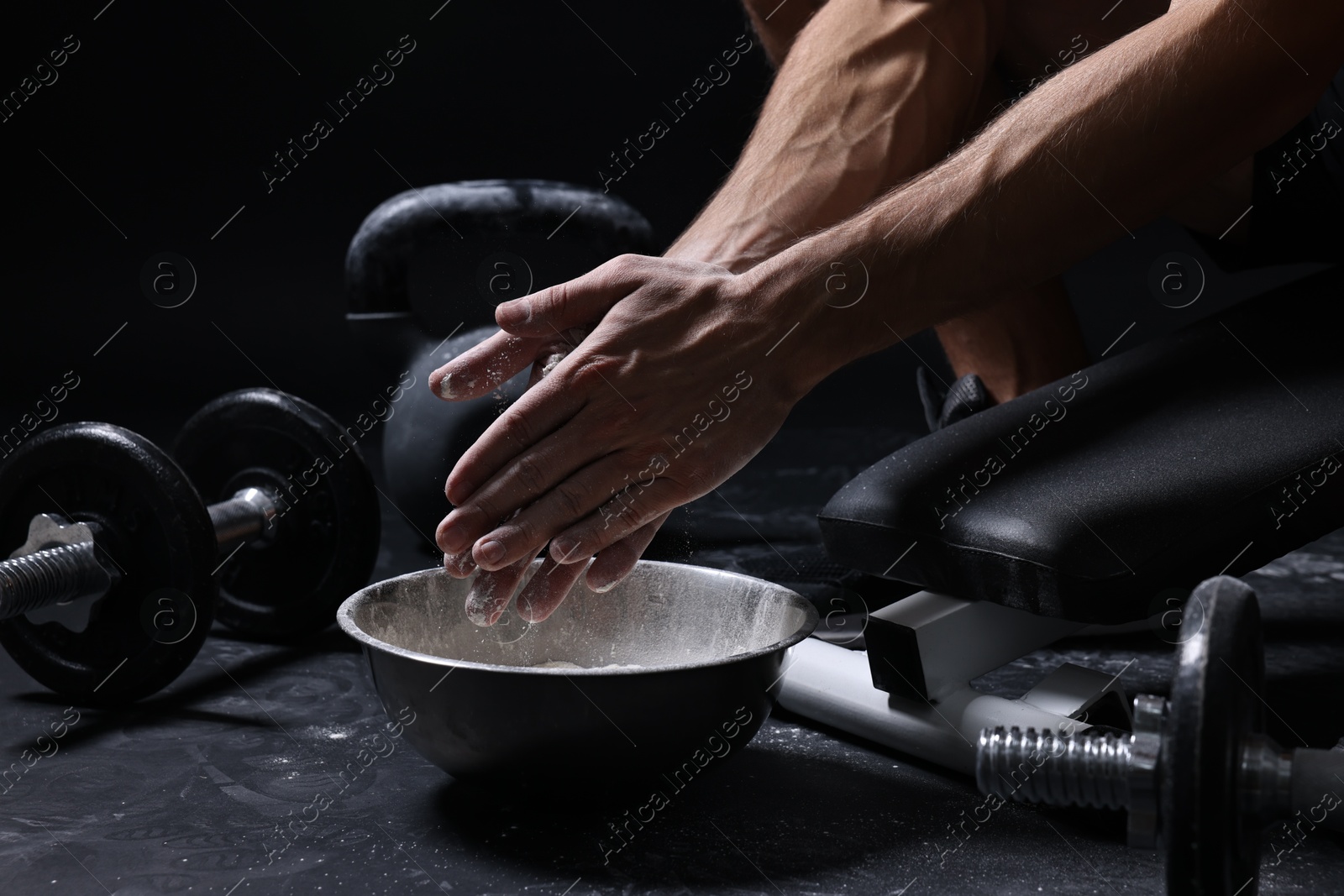 Photo of Man applying talcum powder onto his hands above bowl before training in gym, closeup