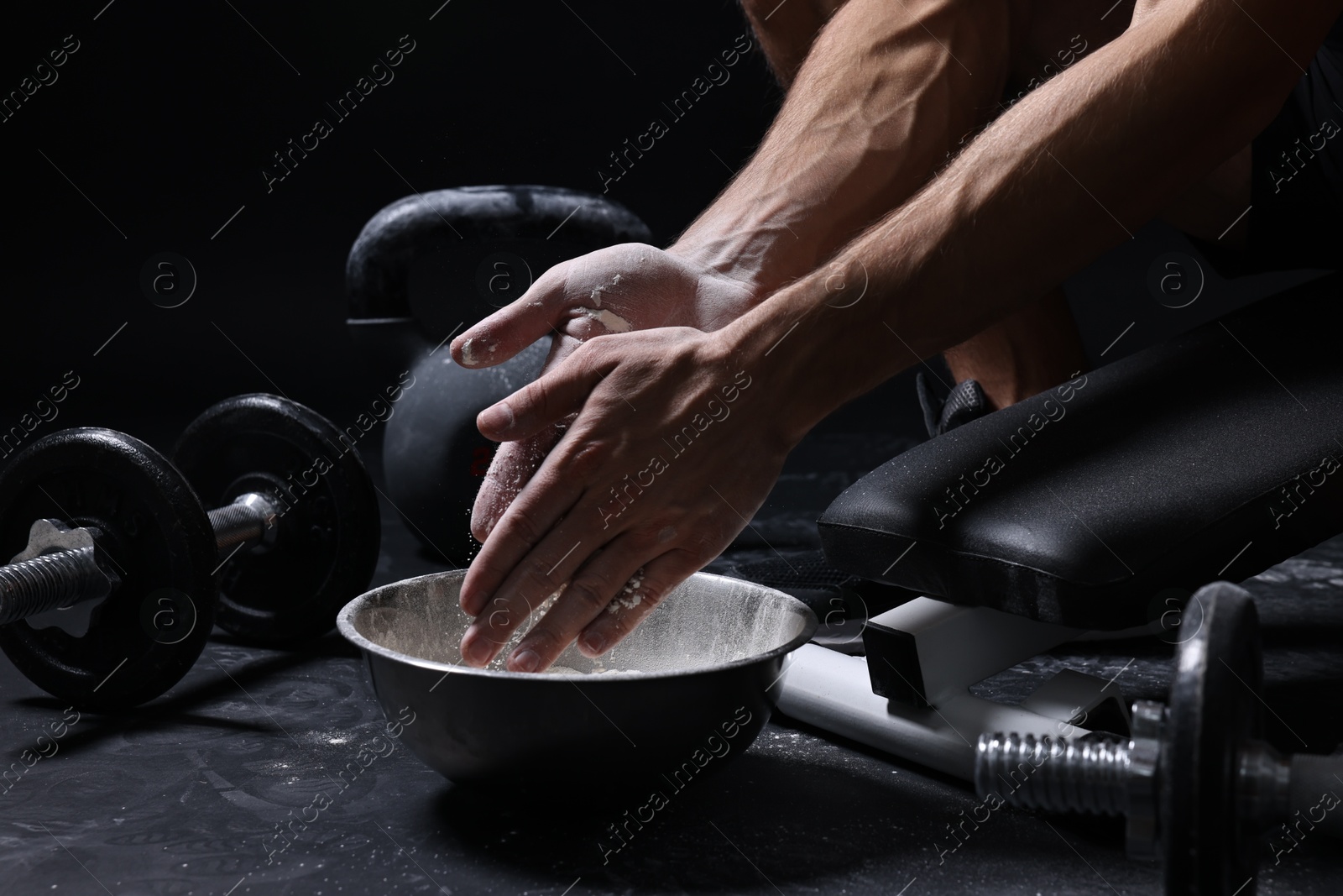 Photo of Man applying talcum powder onto his hands above bowl before training in gym, closeup