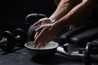 Photo of Man applying talcum powder onto his hands above bowl before training in gym, closeup