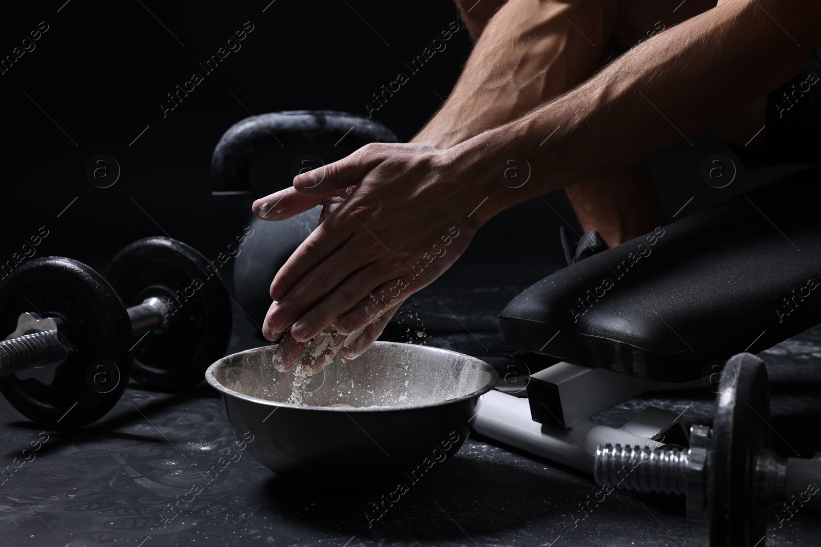 Photo of Man applying talcum powder onto his hands above bowl before training in gym, closeup