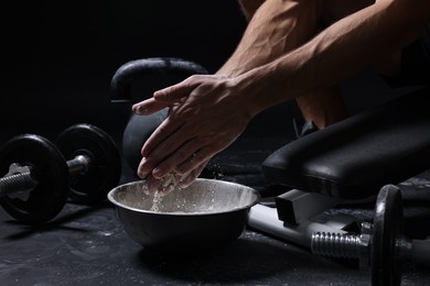 Photo of Man applying talcum powder onto his hands above bowl before training in gym, closeup