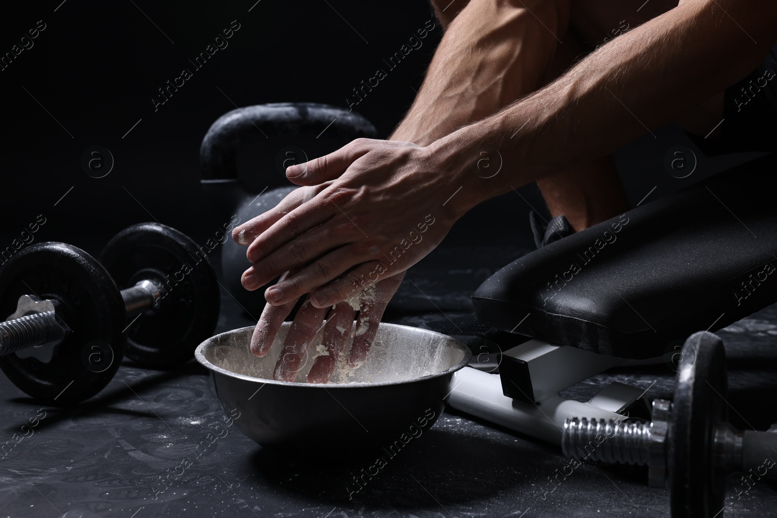 Photo of Man applying talcum powder onto his hands above bowl before training in gym, closeup