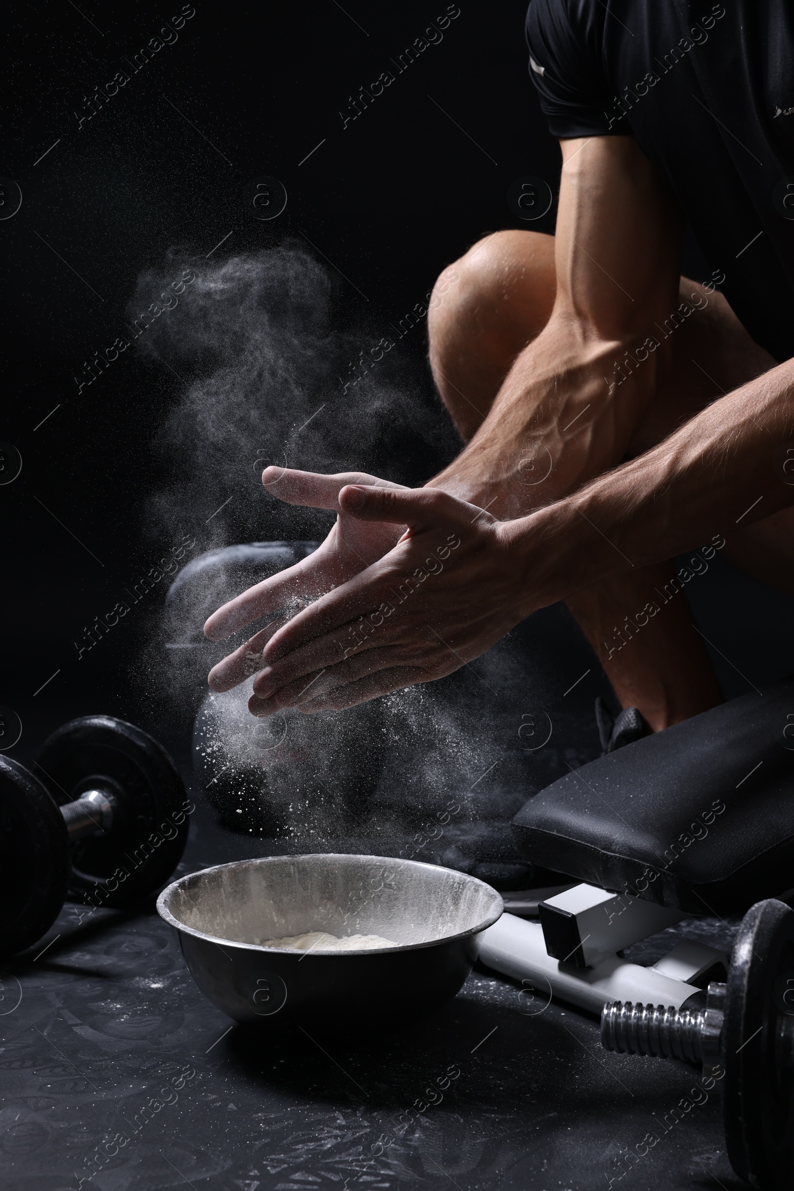 Photo of Man clapping hands with talcum powder above bowl before training on black background, closeup